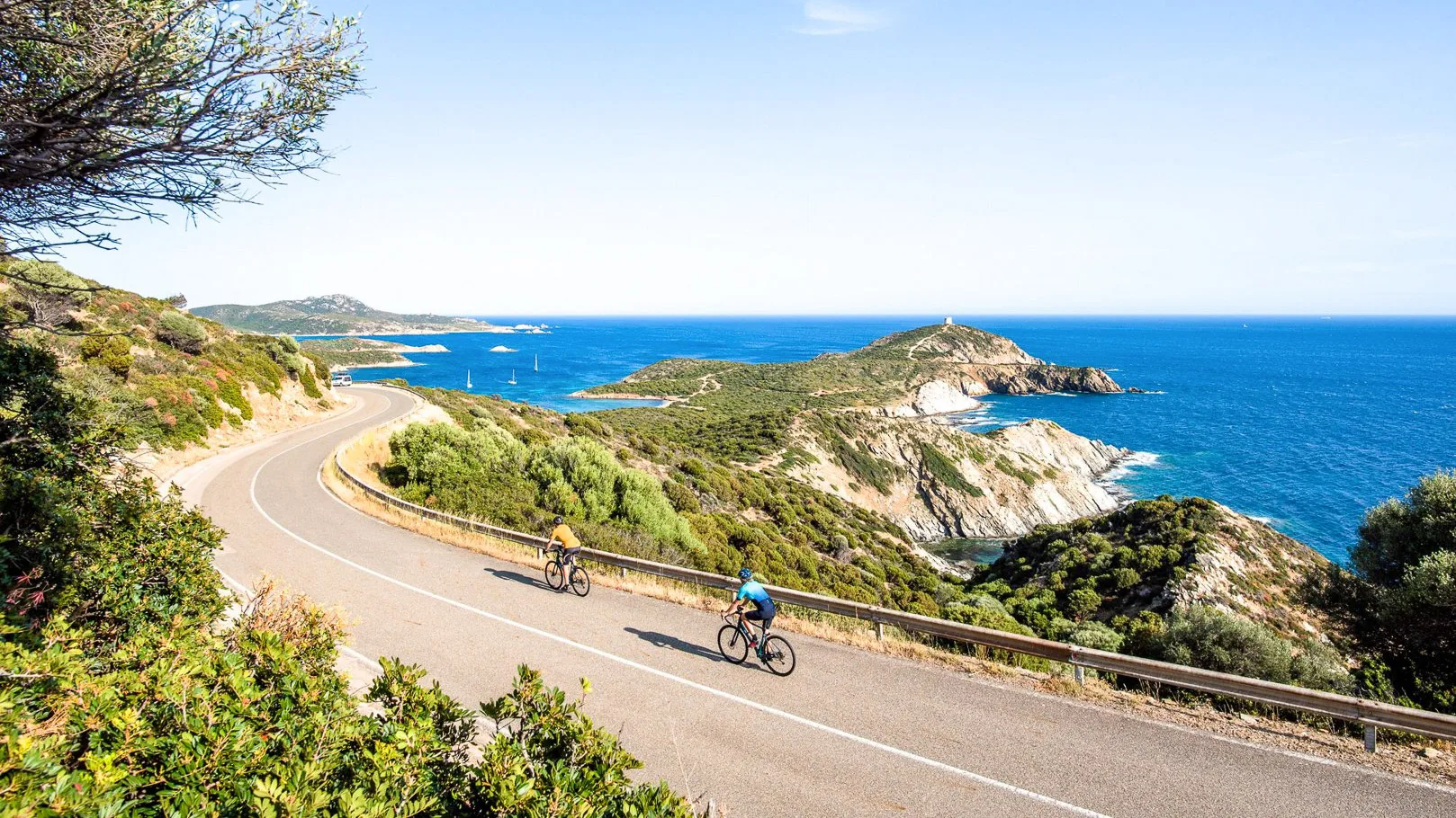 Two cyclists riding along a coastal road in Sardinia with sea views