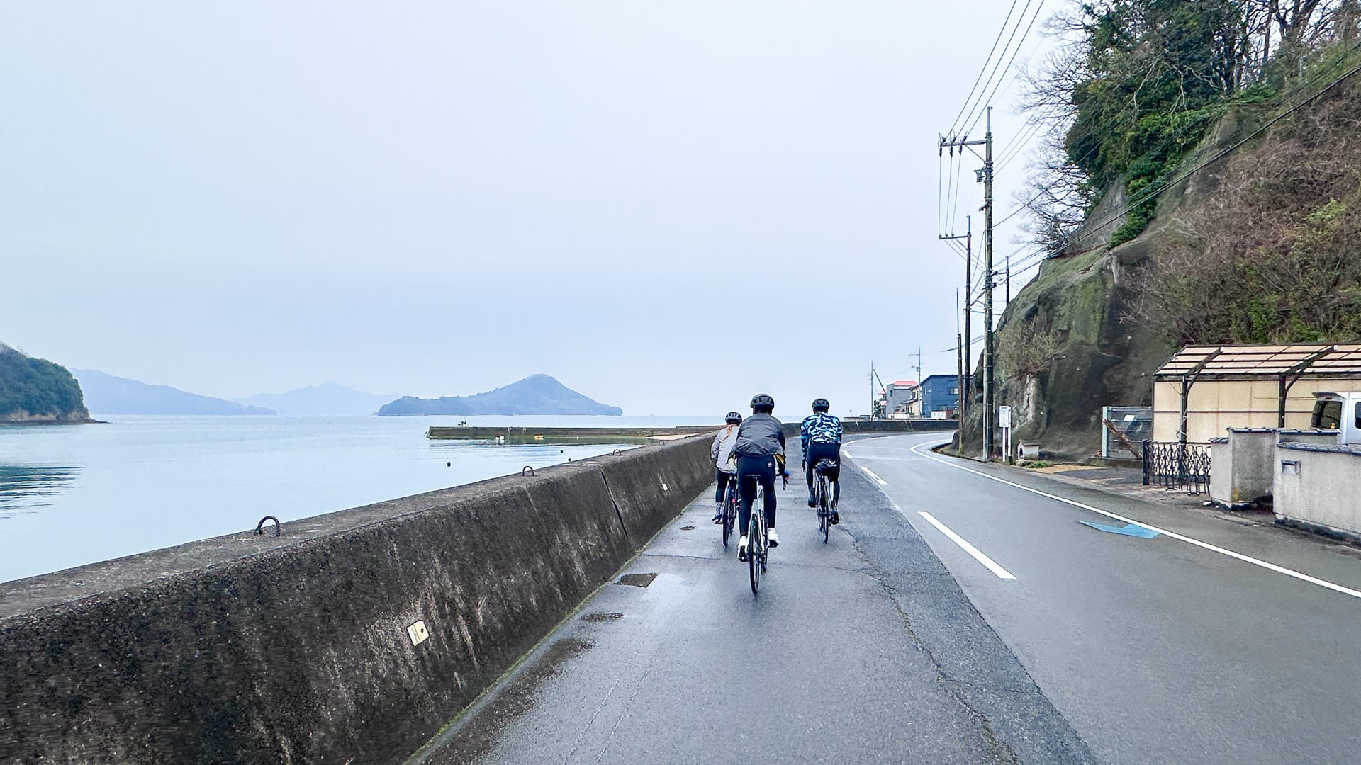 Cyclists riding in rain along south coast of Mukaishima Island, Shimanami Kaido Japan