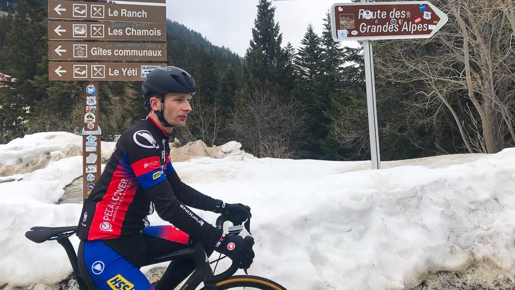 Cyclist in front of Route des Grandes Alpes sign on a mountain road in the French Alps with scenic backdrop