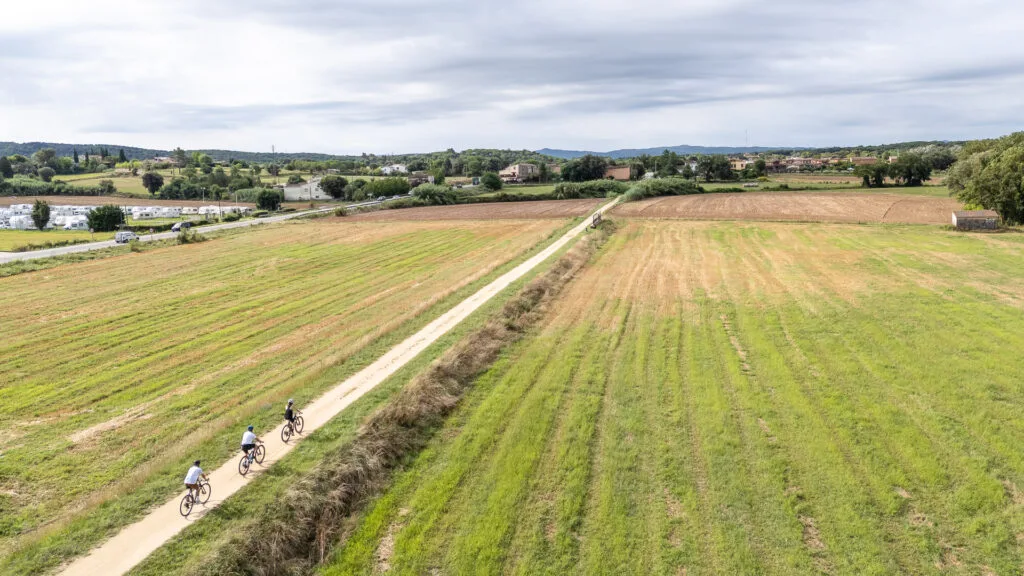 Three cyclists riding along a straight route in Llambilles, Girona