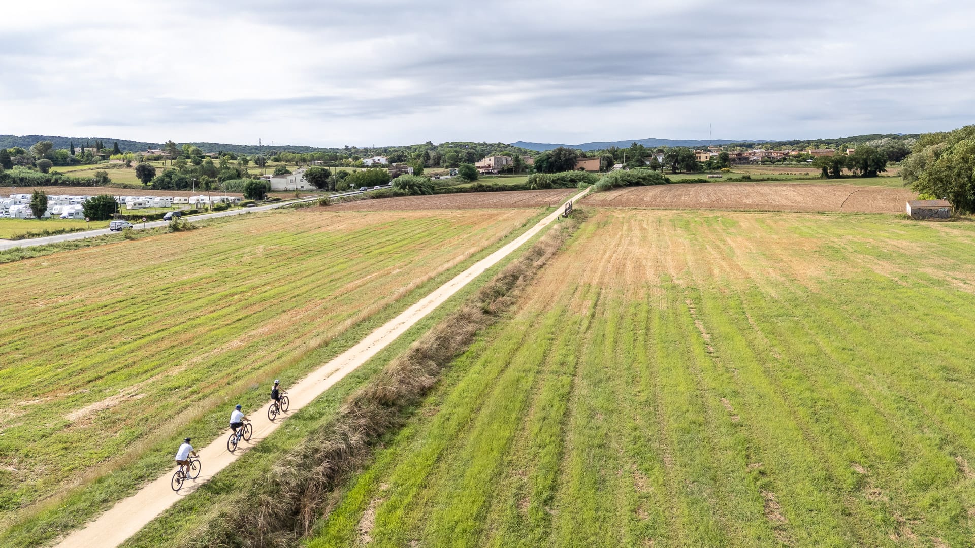 Three cyclists riding along a straight route in Llambilles, Girona