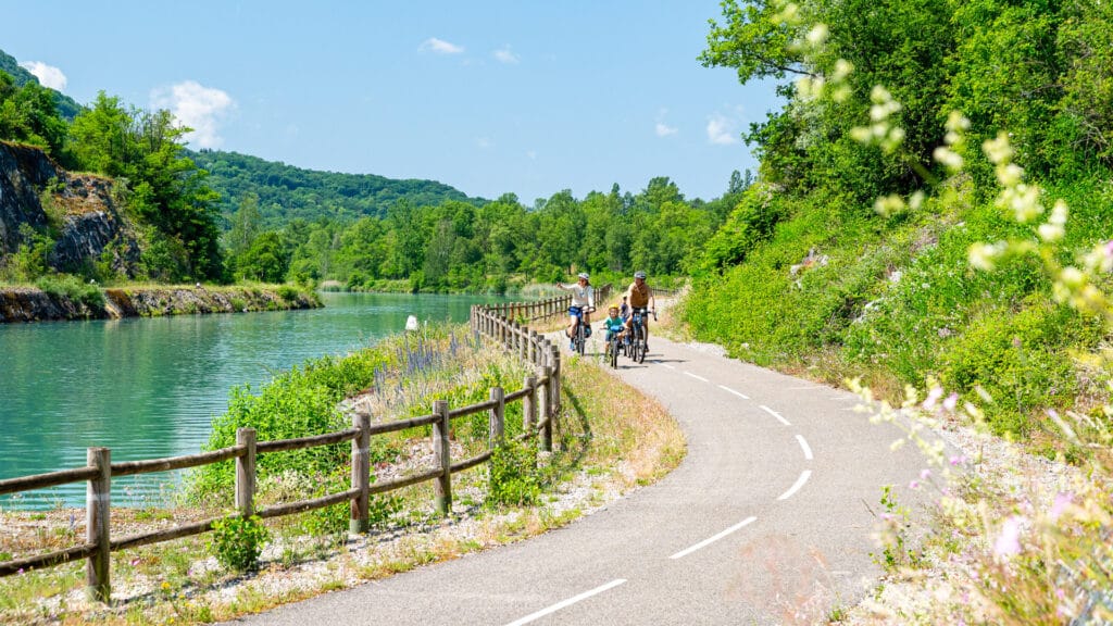 Cyclists riding Le Haut-Rhône around Massignieu-de-Rives, with quiet riverside roads and green countryside