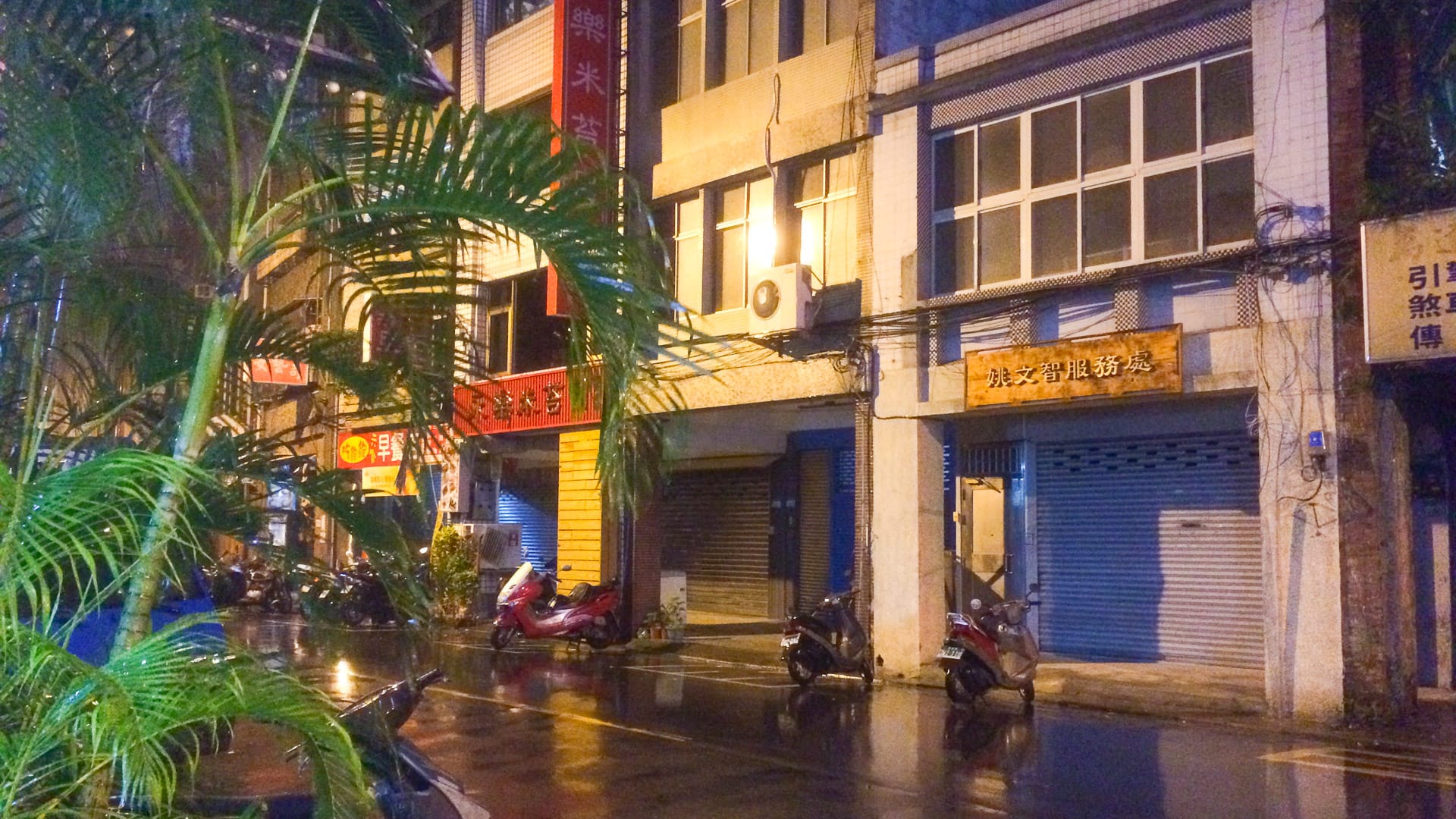 Rain-soaked street in Taipei at night with illuminated shopfronts