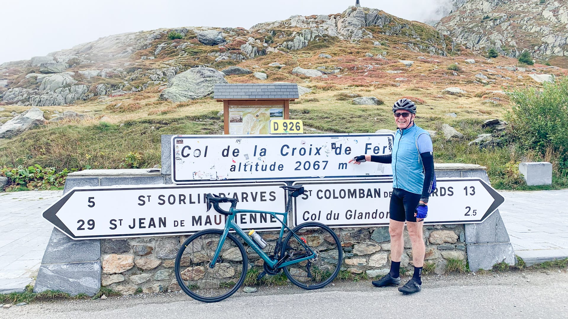 A cyclist taking a photo beside the Col de la Croix de Fer sign