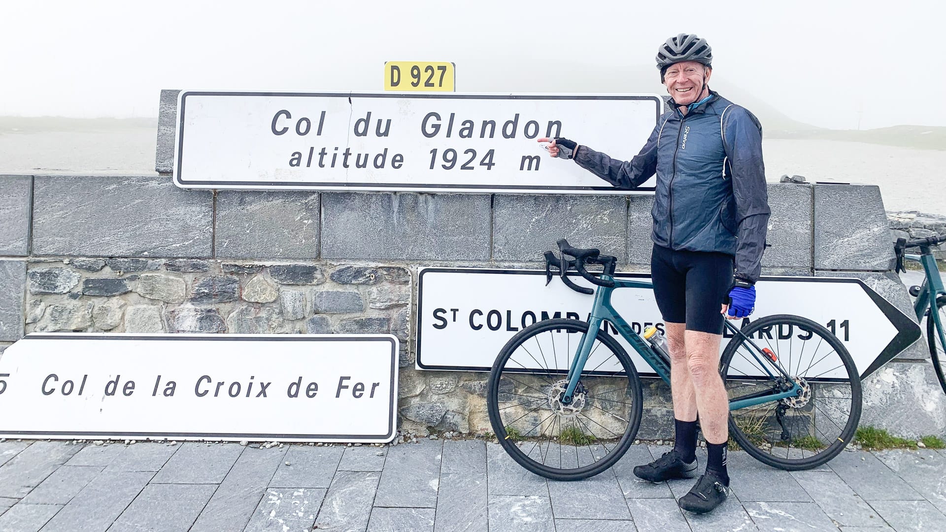 Cyclist taking a photo beside the Col du Glandon sign in the French Alps