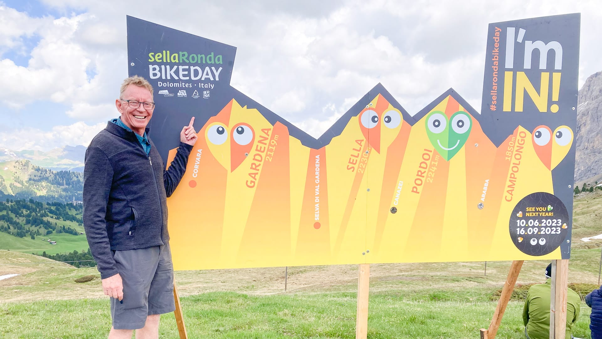 Man taking a photo beside the Sella Ronda Bike Day sign in the Dolomites