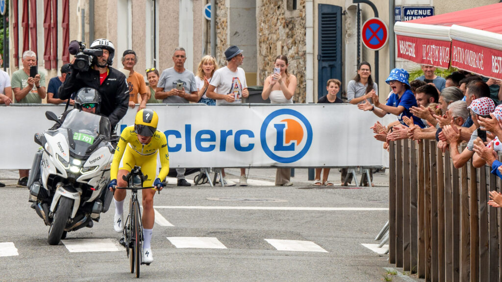 Cyclist Tadej Pogačar in a yellow jersey races past spectators on a Tour de France stage